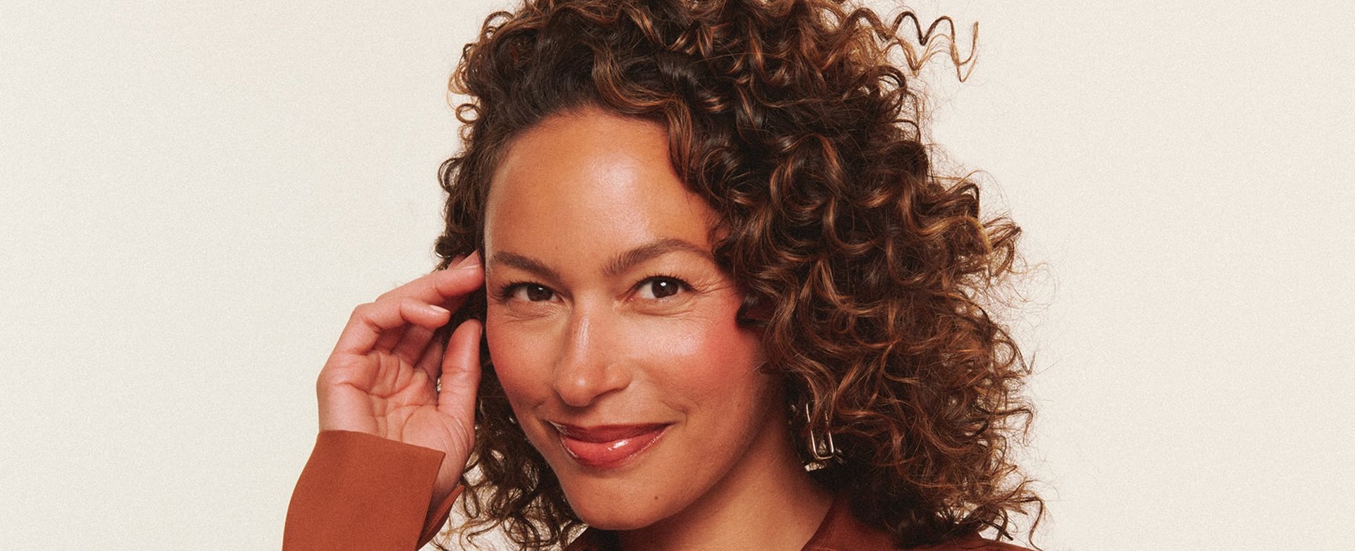 A woman smilng running a hand through brown curly hair