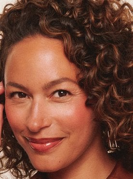 A woman smilng running a hand through brown curly hair